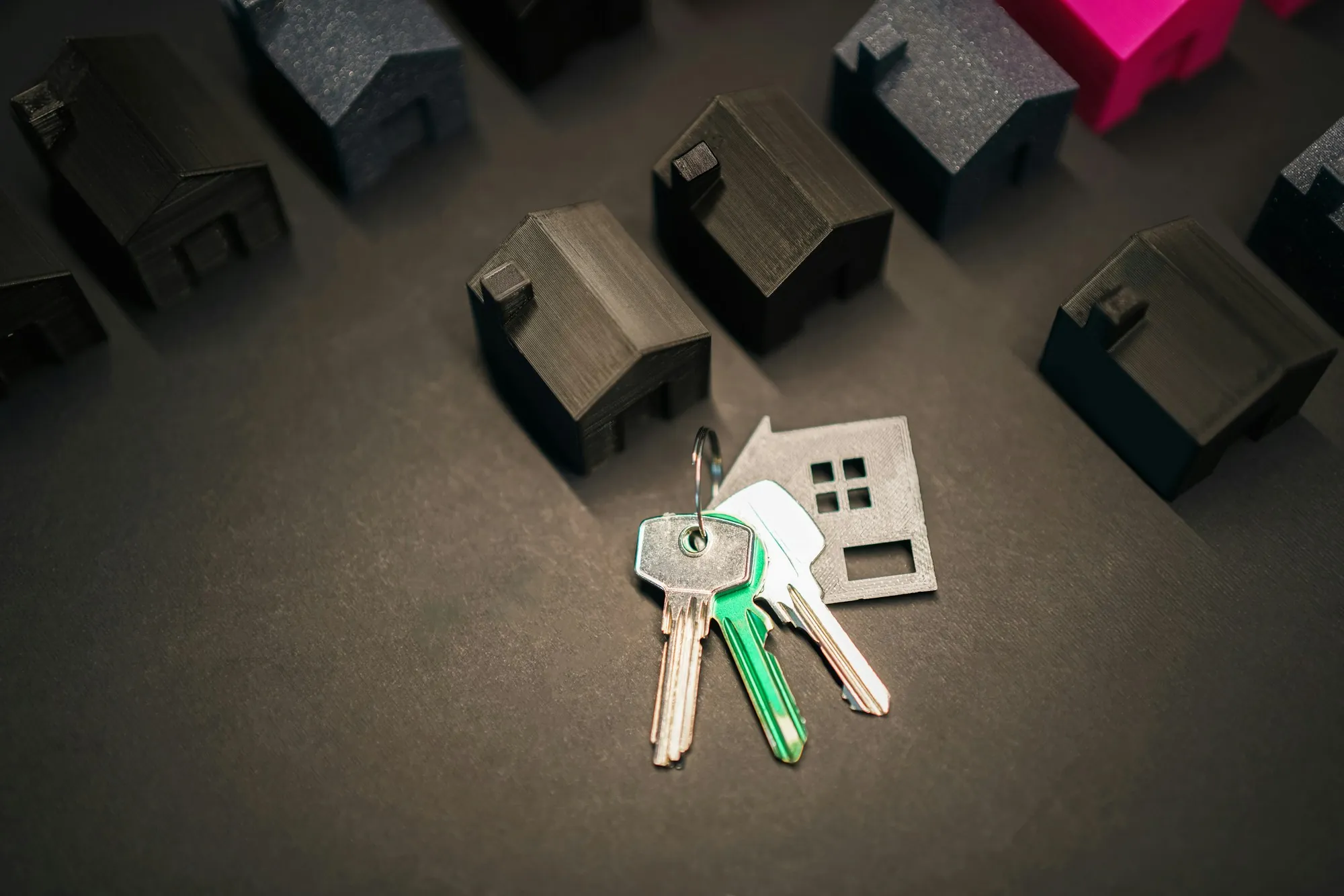 House keys lying beside small model houses on a dark surface