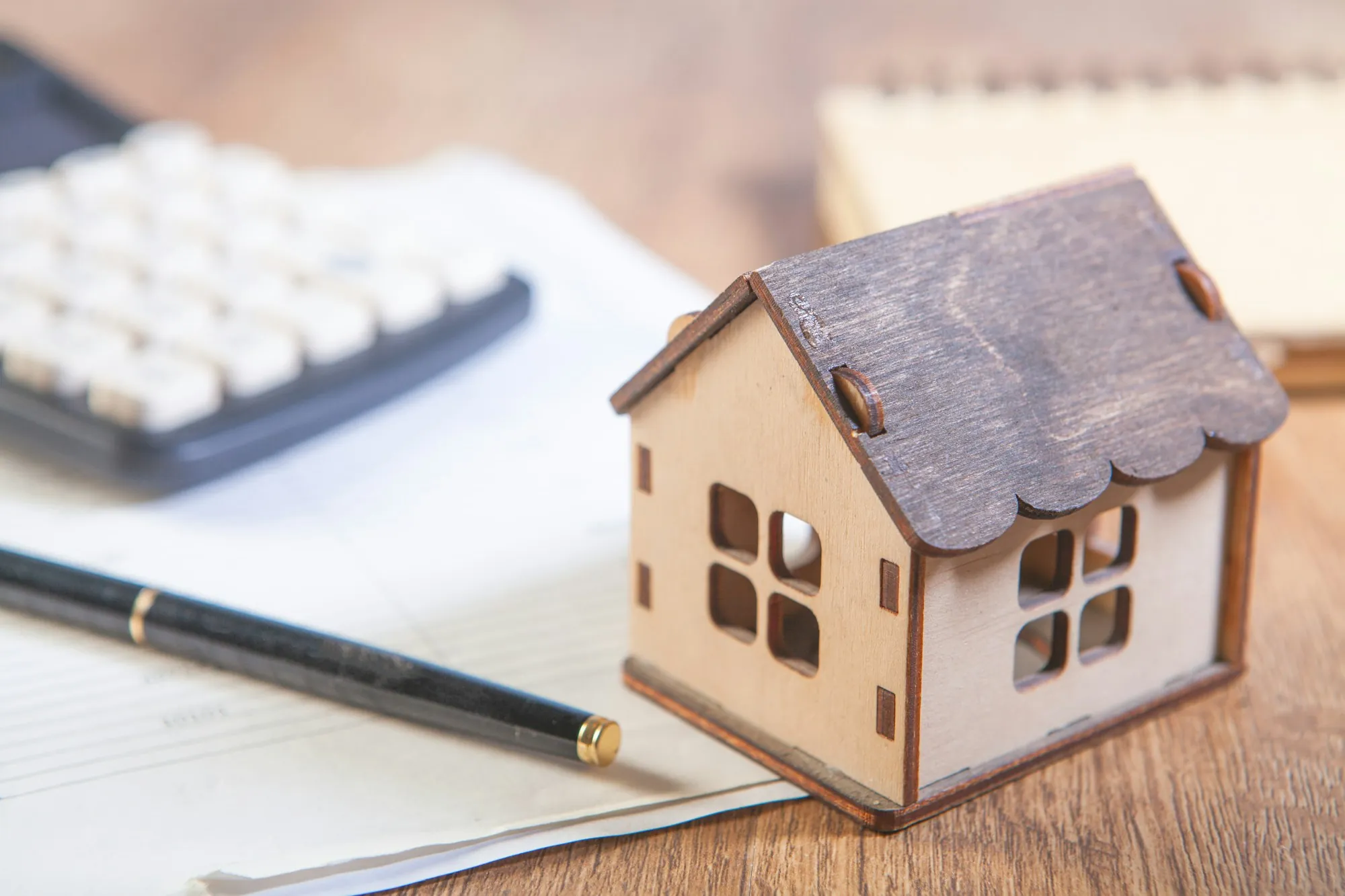 Small wooden model house beside a calculator and pen