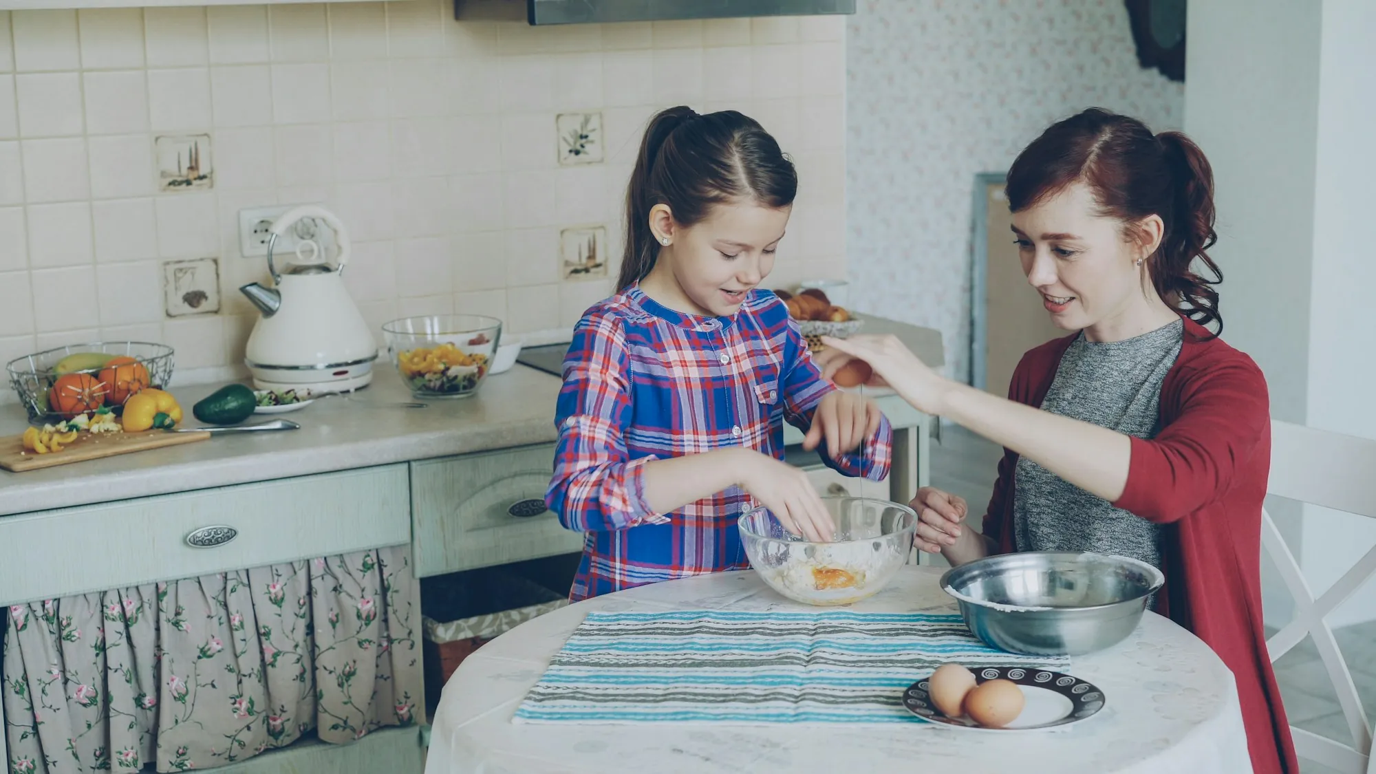 Two girls mixing ingredients in a bowl at a kitchen table